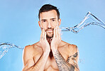 Water splash, skincare and portrait of a man in a studio doing an organic wellness face routine. Beauty, hygiene and male model with natural skin or facial treatment isolated by a blue background.