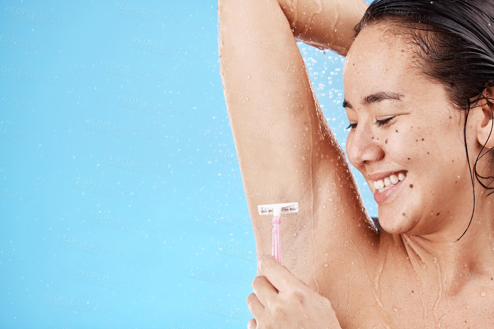 Buy stock photo Shower, underarm and shaving with a model asian woman shaving her armpit in studio on a blue background for grooming. Water, luxury and hair removal with an attractive young female in the bathroom