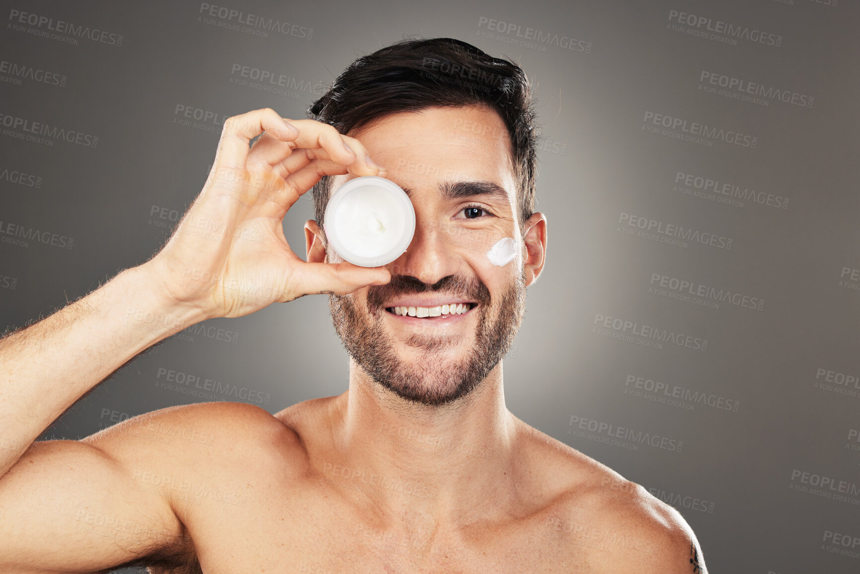 Buy stock photo Face, skincare and product with a man model in studio on a gray background to promote beauty treatment. Portrait, container and antiaging with a handsome young male posing for wellness or care