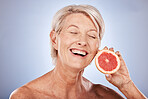 Skincare, beauty and senior woman with a grapefruit for health, wellness and facial beauty against a grey mockup studio background. Excited, happy and elderly model with a smile for a fruit diet