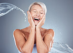 Mature woman, water and splash with shower for clean aesthetic health on a grey background. Beauty, bath and hygiene with a woman washing for bodycare, skincare and wellness for hydration