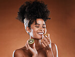 Skincare, beauty and black woman with a kiwi in studio for natural, organic and facial routine. Happy, smell and African girl model with fruit for cosmetic skin treatment isolated by brown background