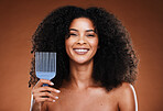 Black woman, hair care and smile in portrait with comb, afro pick and beauty against brown backdrop. Happy African, model and woman with cosmetics, makeup and happiness against studio background