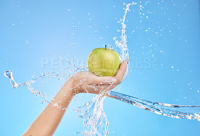 Buy stock photo Hands, fruit and water splash for skincare nutrition, wellness or cosmetics against a blue studio background. Hand holding apple in healthy cleanse, hydration or hygiene for natural vitamin C skin