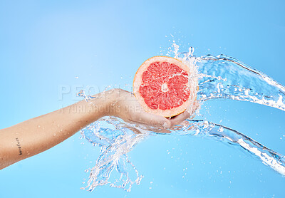 Buy stock photo Hands, fruit and water splash for skincare wellness, cosmetics or nutrition against a blue studio background. Hand holding grapefruit for clean hygiene, hydration or vitamin C for body cleansing