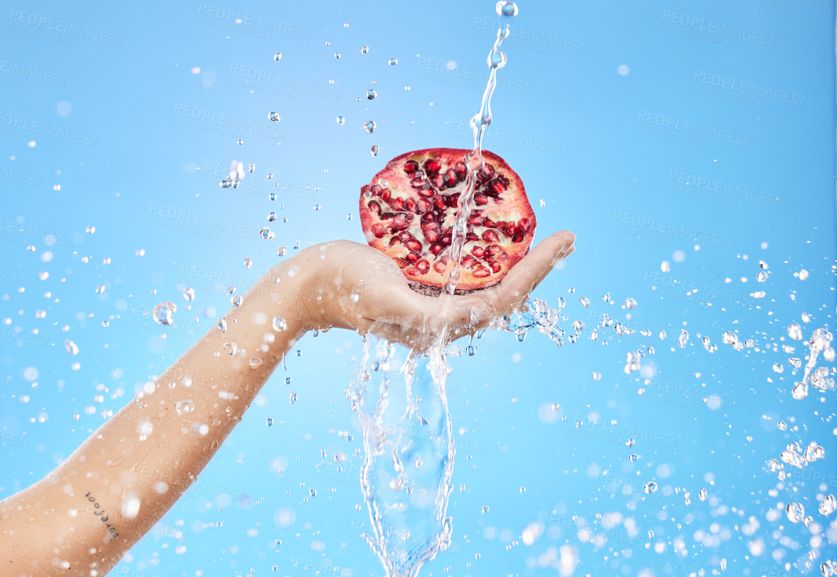 Buy stock photo Water, wellness and hand with pomegranate in studio on blue background for nutrition, diet and healthy lifestyle. Beauty, spa and person holding fruit for skincare products, cosmetics and luxury