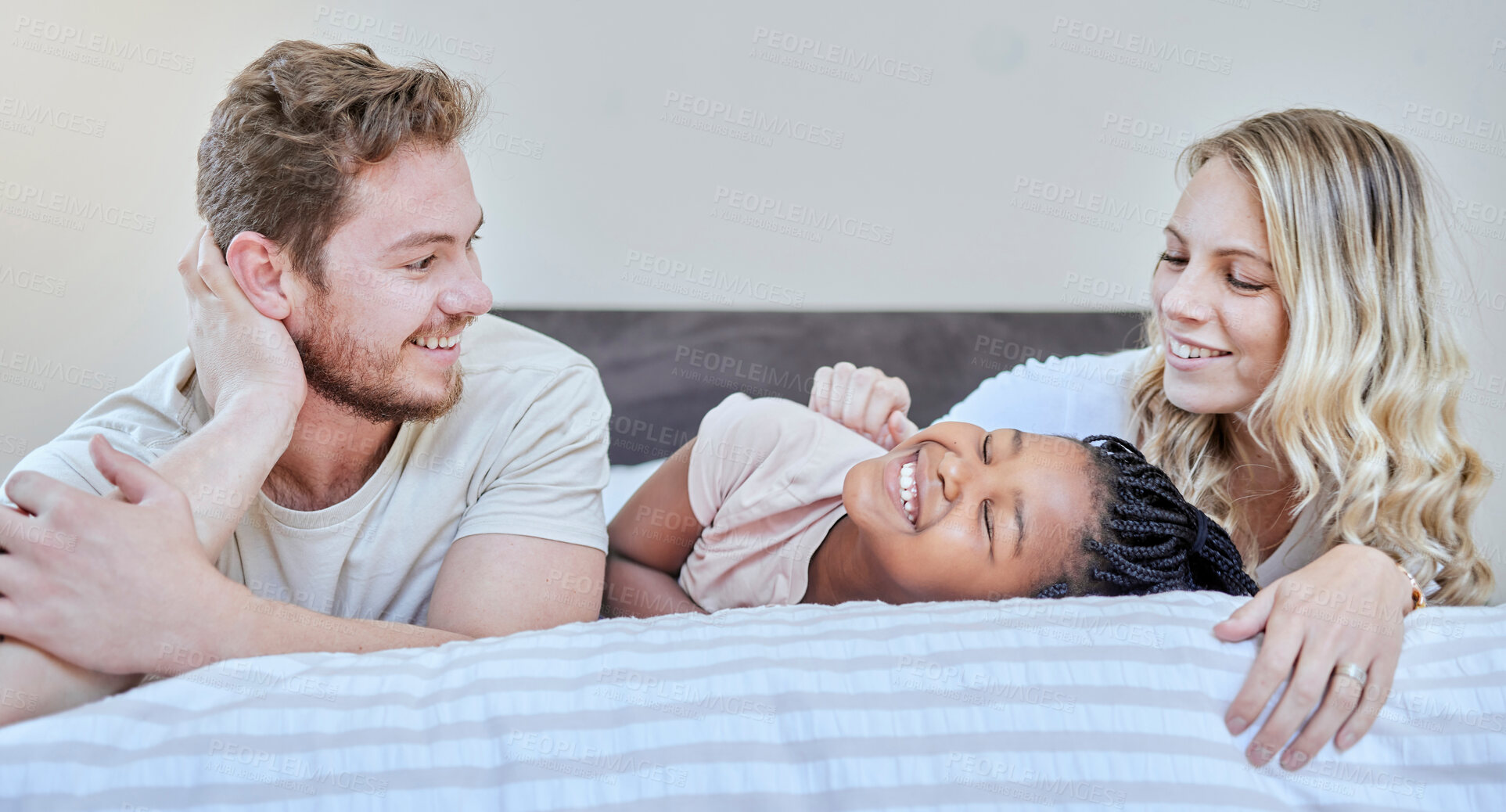 Buy stock photo Family, adoption and love with happy, smile and care together on bed, relax and fun on weekend in home. Diversity, bedroom and happiness with bonding, support and relaxing with moth, father and girl