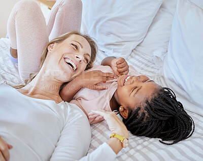 Buy stock photo Happy, adoption and mother relaxing with her child on a bed while talking, laughing and bonding. Happiness, love and mom telling her girl kid a comic joke while lying in the bedroom together at home.