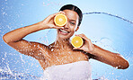 Black woman, fruit and skincare hydration with water splash against blue studio background. Portrait of female holding orange in healthy, natural or organic facial for vitamin C nutrition treatment