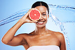 Black woman, grapefruit or smile with water splash for health skincare, wellness or nutrition against a blue studio background. Portrait of happy African American girl with fruit for facial treatment
