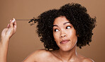 Black woman afro, messy hair and curls looking for cosmetics or salon treatment against a brown studio background. African American female in hair care holding entangled strand on mockup