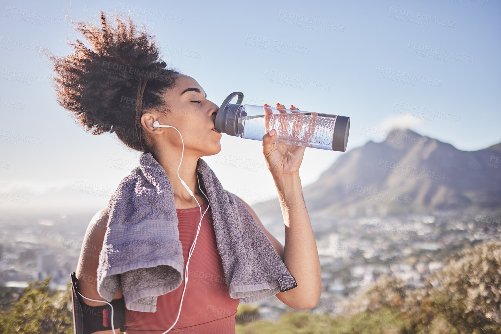 Buy stock photo Music, workout and woman drinking water after exercise at sunrise along mountain, wellness and training on blue sky. Radio, water and black woman stop for break from fitness, running and cardio run