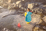 Girl, beach and fishing with net in rock pool, water or ocean with boots, bucket and coat in sunshine. Black child, sea and outdoor for fish, marine life or animal in nature, learning and adventure