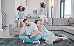 Tired, parents and children jump on sofa with frustrated mom and dad sitting on floor in living room. Family, exhausted couple and playful kids with energy jumping on couch at home during quarantine