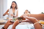 Family, food and lunch at a table with hands of people serving plate with salad for a healthy lifestyle in a dining room at home. Women sitting together while eating a meal for health and wellness