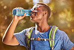 Fitness, hiking and black man with water bottle for hydration while outdoor in nature with backpack for travel, trekking and adventure. Thristy male in a forest for a hike, workout and training