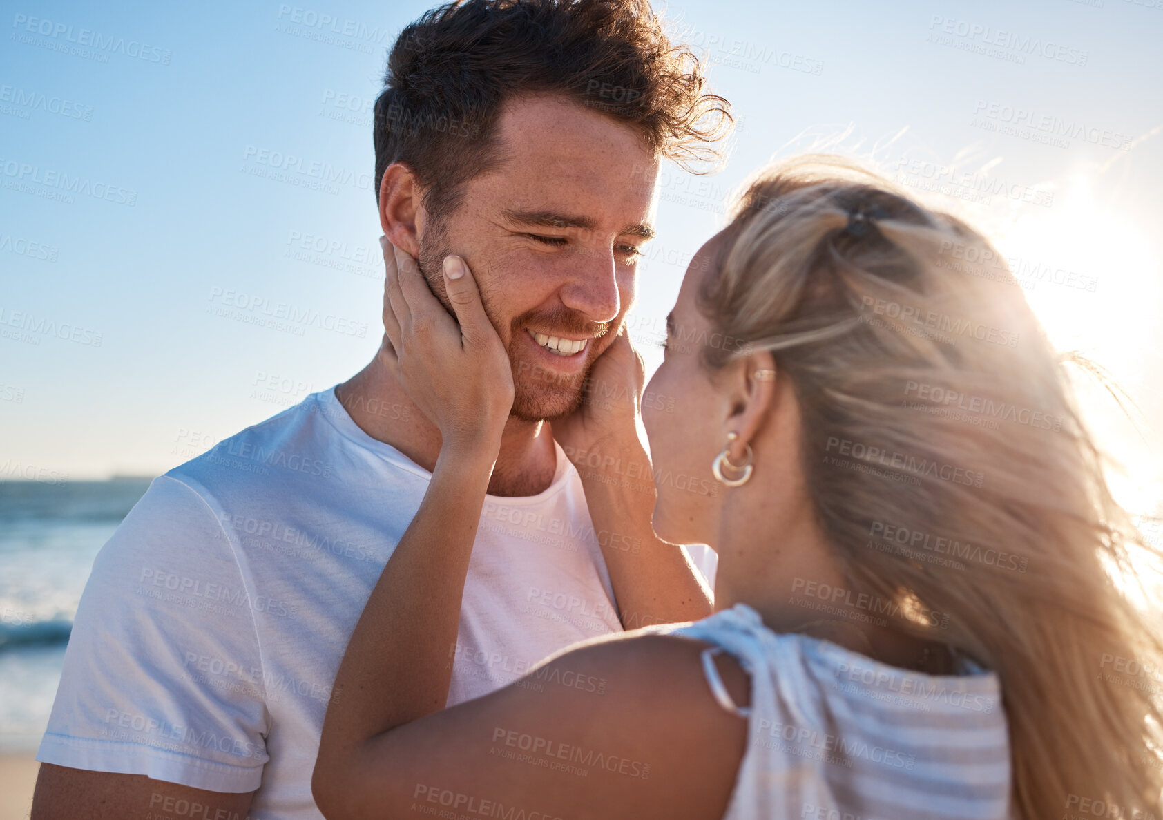 Buy stock photo Woman, man and touch face, love and happy together at the beach, travel and romance outdoor for bonding. Couple on adventure by the ocean, embrace with lens flare and care while spending quality time