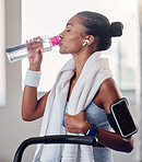Drinking water, fitness and smartphone on woman arm gym gear, technology and listening to music for workout on stationary cycling machine. Tired, challenge and motivation black woman cardio training