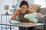 Woman, detergent and smile for cleaning table, hygiene or sanitary wiping in the living room at home. Female spraying anti bacterial liquid cleaner on wooden desk for health safety and hygienic house