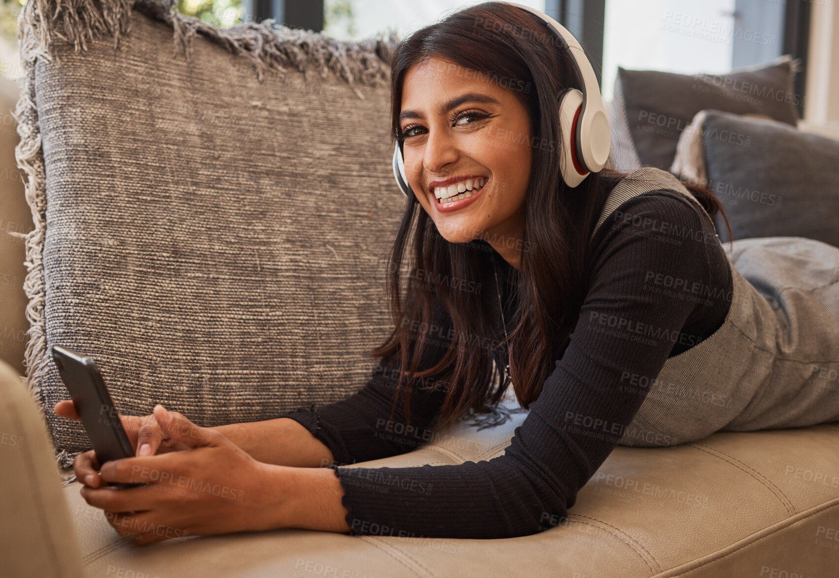 Buy stock photo Woman, happy and headphone phone music of a person listening to a podcast or video watching at home. Portrait of an indian person with happiness and smile about mobile technology on living room sofa