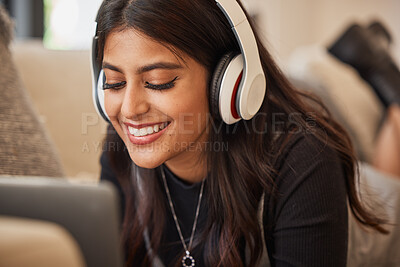 Buy stock photo Laptop, music and headphones with an indian woman listening to audio in the living of her home. Podcast, streaming and subscription service with a young female typing on her computer on the sofa