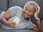 Black woman, music and phone video streaming in a home living room on a sofa happy. Social media app scroll, internet and mobile web podcast watching with headphones and happiness in a house