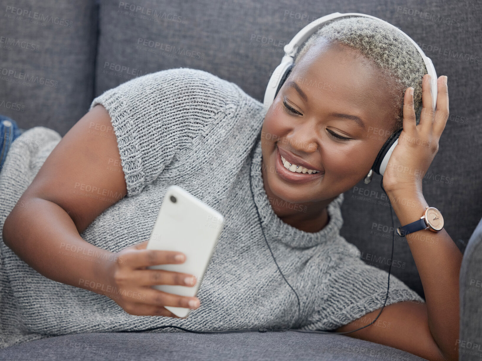 Buy stock photo Black woman, music and phone video streaming in a home living room on a sofa happy. Social media app scroll, internet and mobile web podcast watching with headphones and happiness in a house