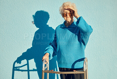 Buy stock photo Portrait, shadow and disability with a senior woman on a blue wall background while holding a mobility walker outdoor. Health, handicap and fashion with a mature female standing outside alone