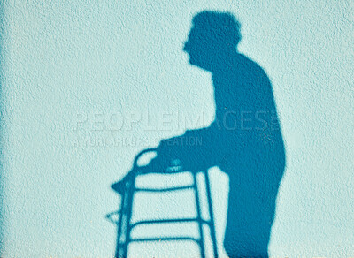 Buy stock photo Shadow, disability and walking with a senior woman outdoor on a blue wall background on a sunny summer day. Silhouette, handicap and mobility walker with a mature female outside alone for a walk
