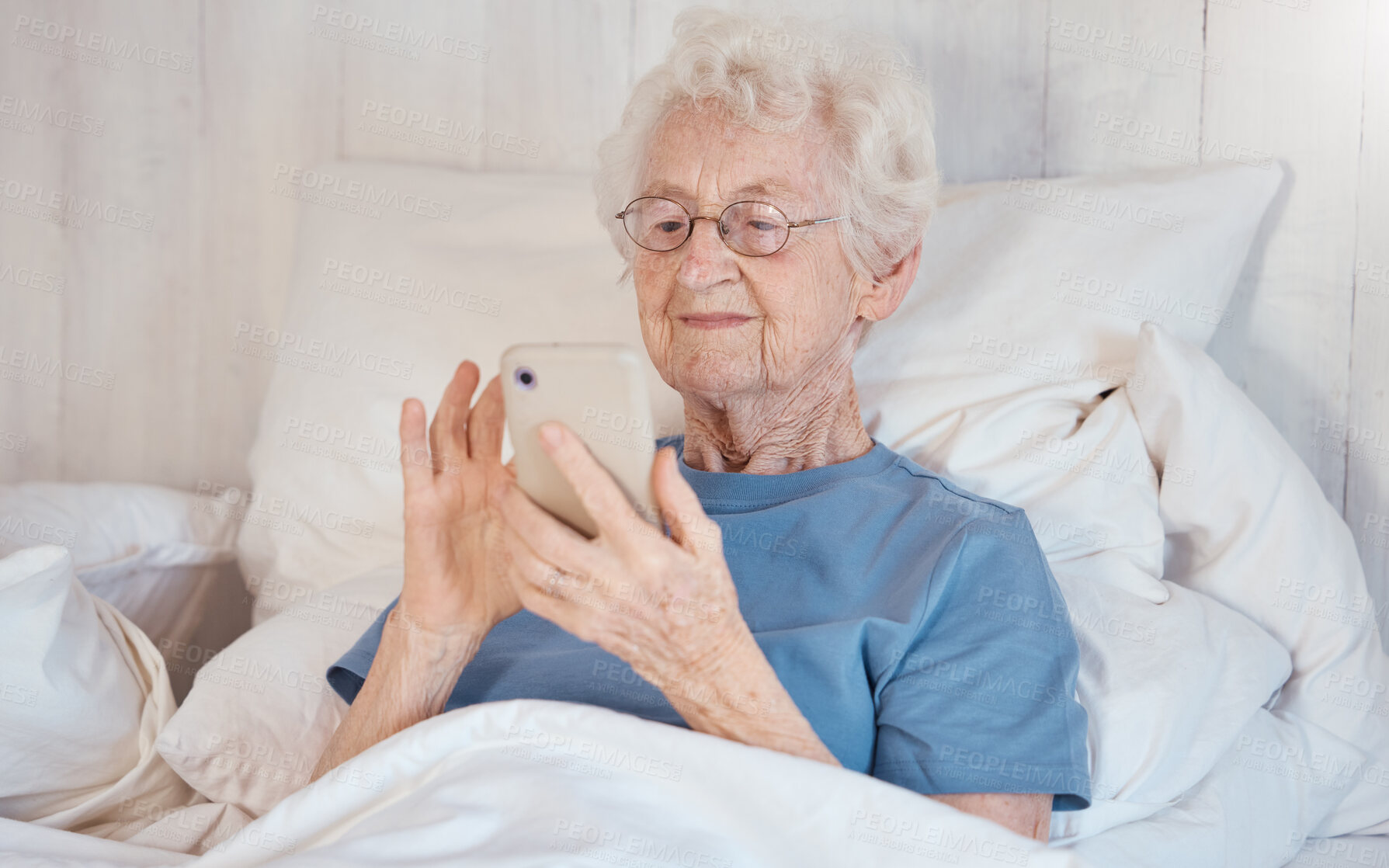 Buy stock photo Phone, bed and senior woman in nursing home surfing internet, social media or nostalgic photographs with happy memories. Communication, technology and grandma in bedroom of retirement home with smile