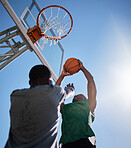 Basketball player, low angle and competition games on blue sky background of outdoor sports, fitness and energy for goals, performance and action. Basketball hoop, friends and men, court and training