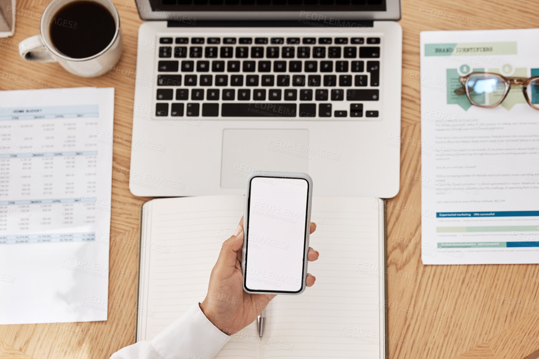 Buy stock photo Laptop, paperwork and phone with mockup space at a desk in a modern office working on project. Cup of coffee, computer and hand holding a smartphone with blank screen with copy space in the workplace