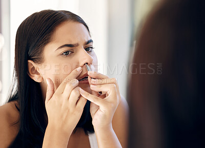 Buy stock photo Face, nose and beauty with a woman using a tweezer to remove nasal hair in the bathroom of her house. Mirror, reflection and grooming with an attractive young female tweezing her nostrils at home