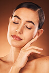 Skincare, facial and hands of woman on face in studio for beauty, makeup and hygiene wellness on orange background. Hand, girl and model in India for cosmetic, product and smooth skin care mock up
