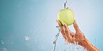 Water splash, hand of woman and apple in studio on a blue background mockup. Fresh food, cleaning hygiene and female model washing fruit for healthy diet, vitamin c or nutrition, skincare or beauty.