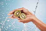 Water splash, hands of woman and kiwi in studio on a blue background. Cleaning, hygiene and female model washing fruits for healthy diet, nutrition and vitamin c for skincare, beauty and wellness.