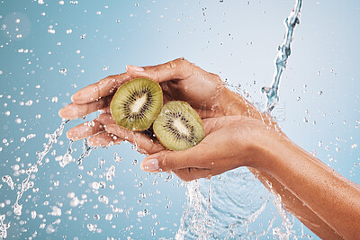 Buy stock photo Water splash, hands of woman and kiwi in studio on a blue background. Cleaning, hygiene and female model washing fruits for healthy diet, nutrition and vitamin c for skincare, beauty and wellness.