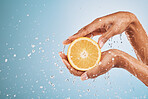 Orange, woman hands and water splash for beauty, vitamin c detox and natural skincare, healthy cosmetics and body wellness on studio blue background. Closeup of clean, wet and shower on citrus fruits