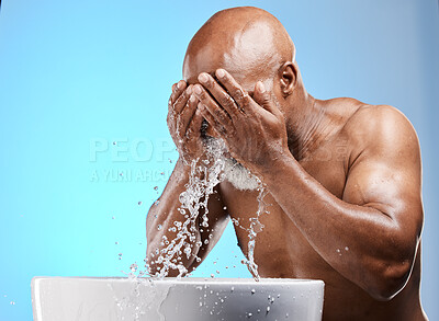 Buy stock photo Water splash, face and black man in studio for beauty, skincare and cosmetics glow, shine and wellness promotion on blue background. Cleaning, facial and water drops in bathroom and marketing space