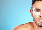 Portrait, skincare and man with eye mask in studio for beauty, grooming and hygiene wellness on blue background.  Face, facial and model relax with eye patch, collagen and skin, cleaning and product 