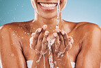 Water splash, skincare and black woman with wellness, wet and smile. Hands, liquid drops and young female with body care, health and on blue studio background for natural beauty, smooth or clear skin