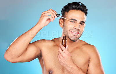 Buy stock photo Man, face serum or skincare grooming on studio background for healthcare wellness, dermatology routine or acne treatment. Portrait, smile or happy Indian model with facial oil product on blue mock up
