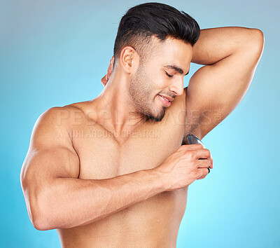 Buy stock photo Grooming, armpit and man shaving body hair for hygiene, health and wellness on a blue studio background. Indian model for epilation with electric shaver for hair removal for clean underarm and skin