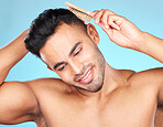 Hair care, beauty and man brushing hair, marketing barber and salon care against a blue background in studio. Self care, grooming and model thinking of hairstyle with a brush for advertising