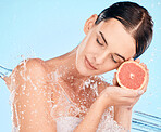 Beauty, splash and water with a woman holding fruit for health, skincare and wellness on a blue studio background. Clean, shower and cosmetics with a grapefruit for vitamin c skin care and bodycare 