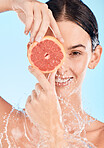 Woman, skincare and grapefruit with smile, water splash and beauty in studio for wellness by backdrop. Happy model, cosmetic fruit and splash for moisturizer, skin and healthy face by blue background