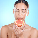 Face, skincare and woman with grapefruit and eyes closed in studio isolated on a blue background. Wellness, food or female model holding healthy fruit for natural vitamin c, nutrition or healthy skin