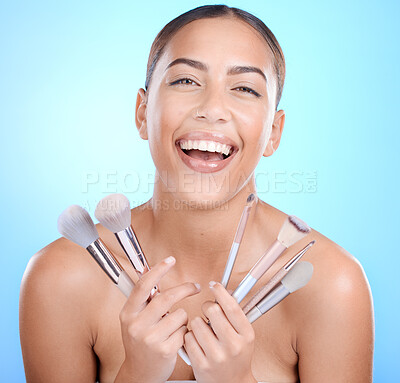 Buy stock photo Woman, beauty portrait and brushes for makeup, skincare or cosmetics with happy smile by blue background. Model, cosmetic brush or tools for facial, skin or aesthetic on face with happiness in studio
