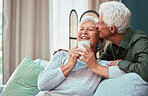 Kiss, coffee and senior couple laughing, talking and smile during retirement in the living room of their house. Relax, love and elderly man and woman with affection, tea drink and comic conversation