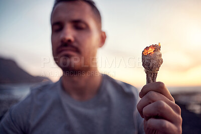 Buy stock photo Man, hand and burning sage on the beach while meditating for spiritual peace and zen mindfulness. Herb, burn and alternative cleanse ceremony to meditate for smudge during a seaside peaceful time